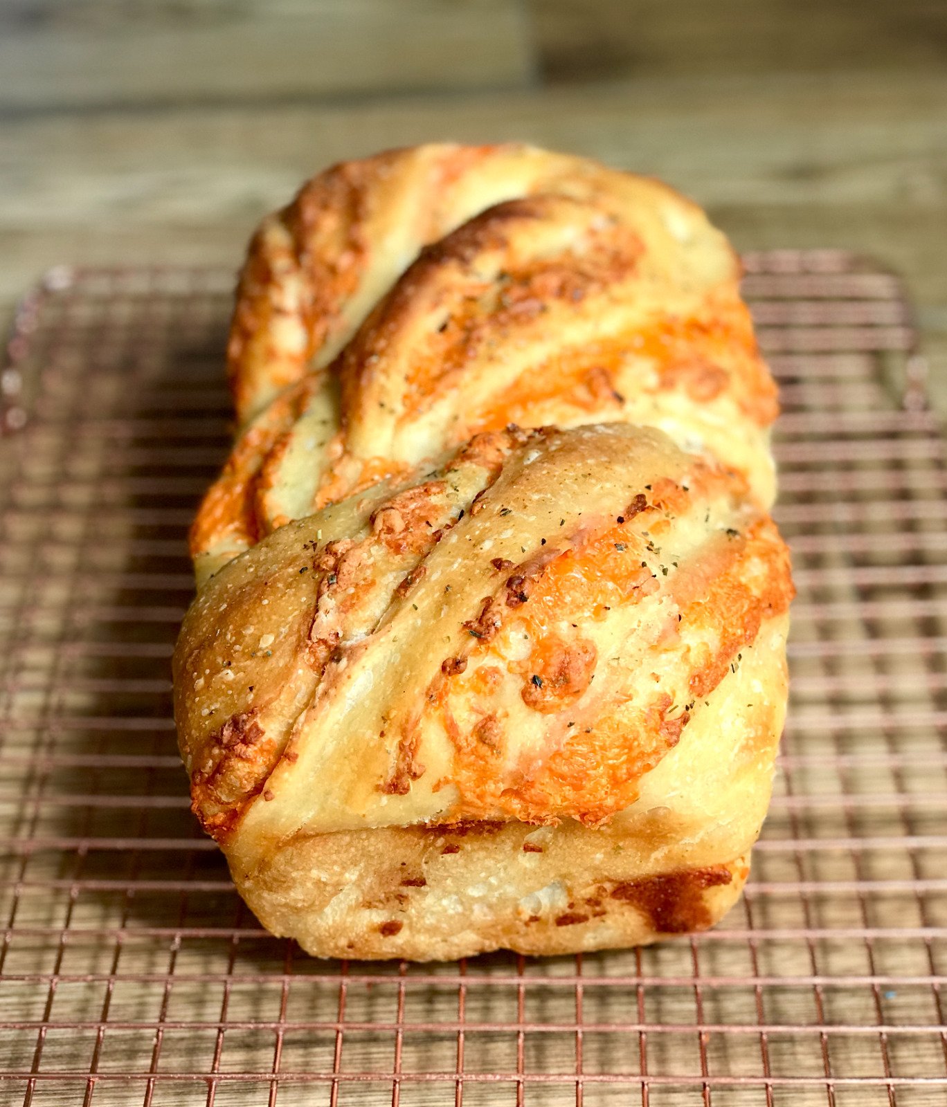 A cheesy garlic sourdough loaf braided with melted cheddar and dusted with herbs on a copper rack