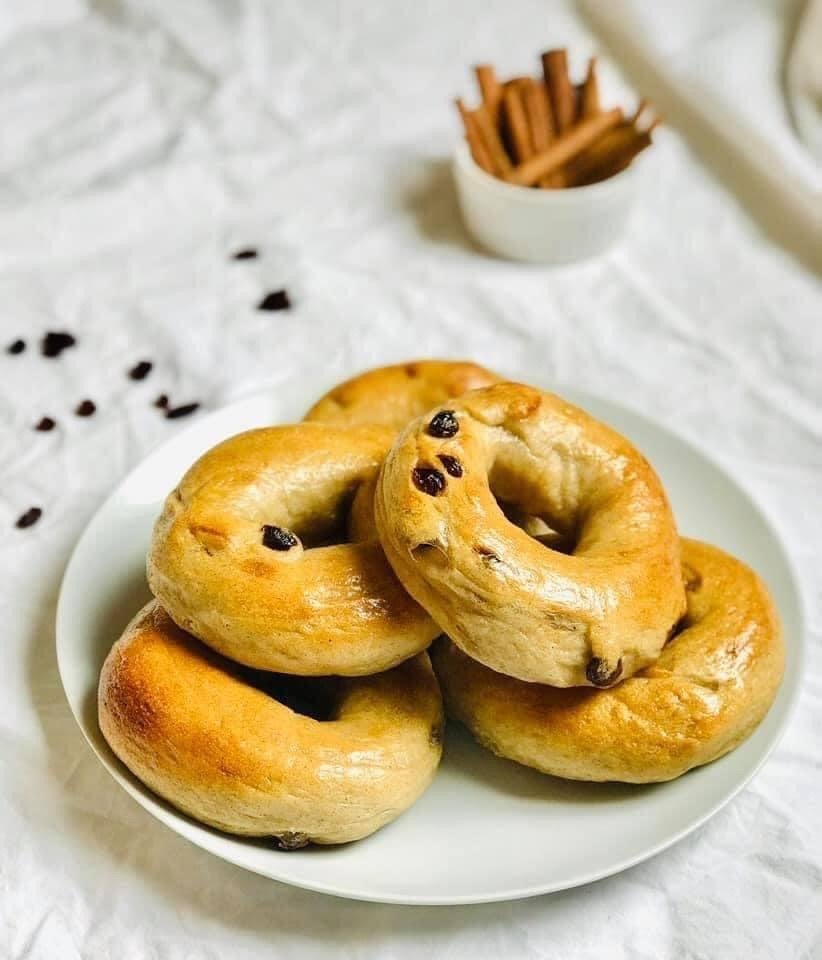 A plate of cinnamon-raisin sourdough bagels with cinnamon sticks and scattered raisins