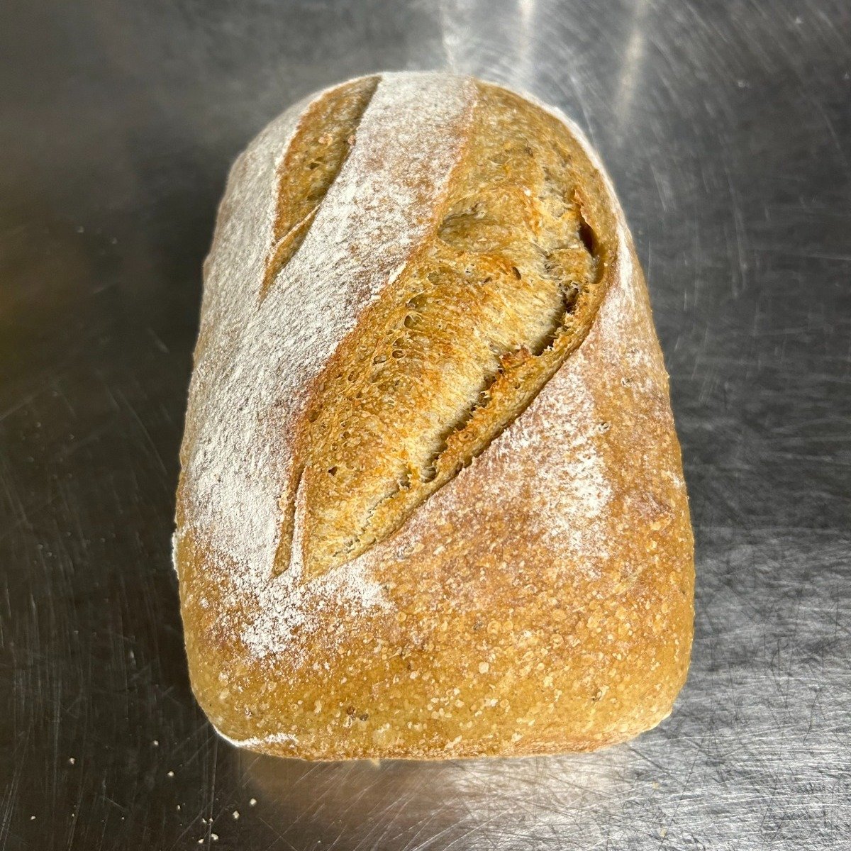 A rustic dark rye sourdough loaf, deeply scored and dusted with flour, on stainless steel