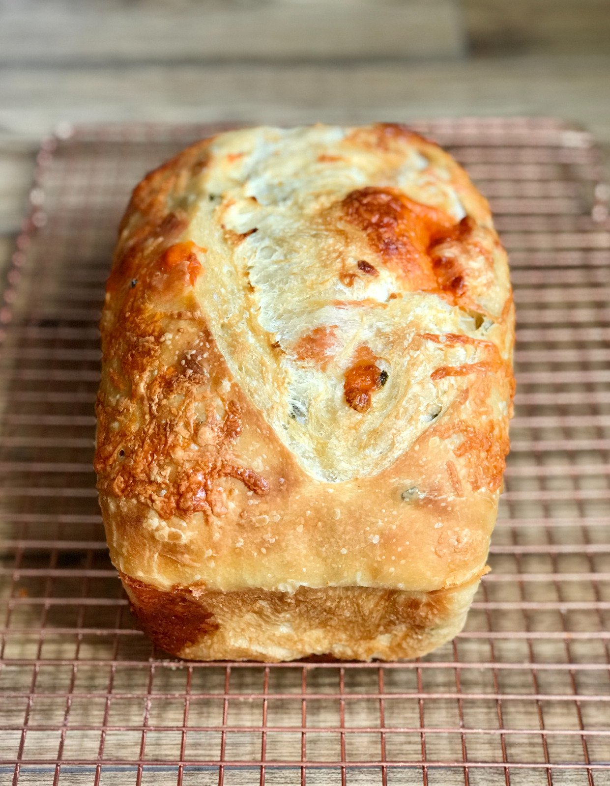 A jalapeéo cheddar sourdough loaf with melted cheese and pepper flecks across a golden crust