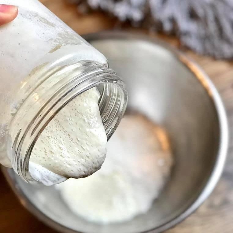 Bubbling, active sourdough starter poured from a jar into a metal bowl