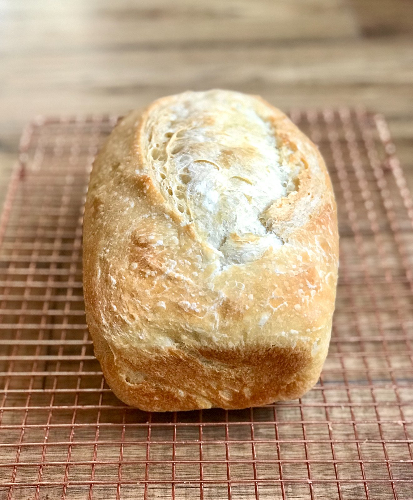 A pale, crackly-crusted white sourdough loaf cooling on a wire rack